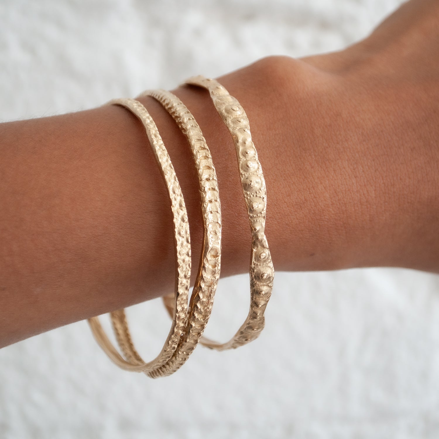 Textured gold bangles on a wrist against a white background - Lauren Wolf Jewelry | ESQUELETO